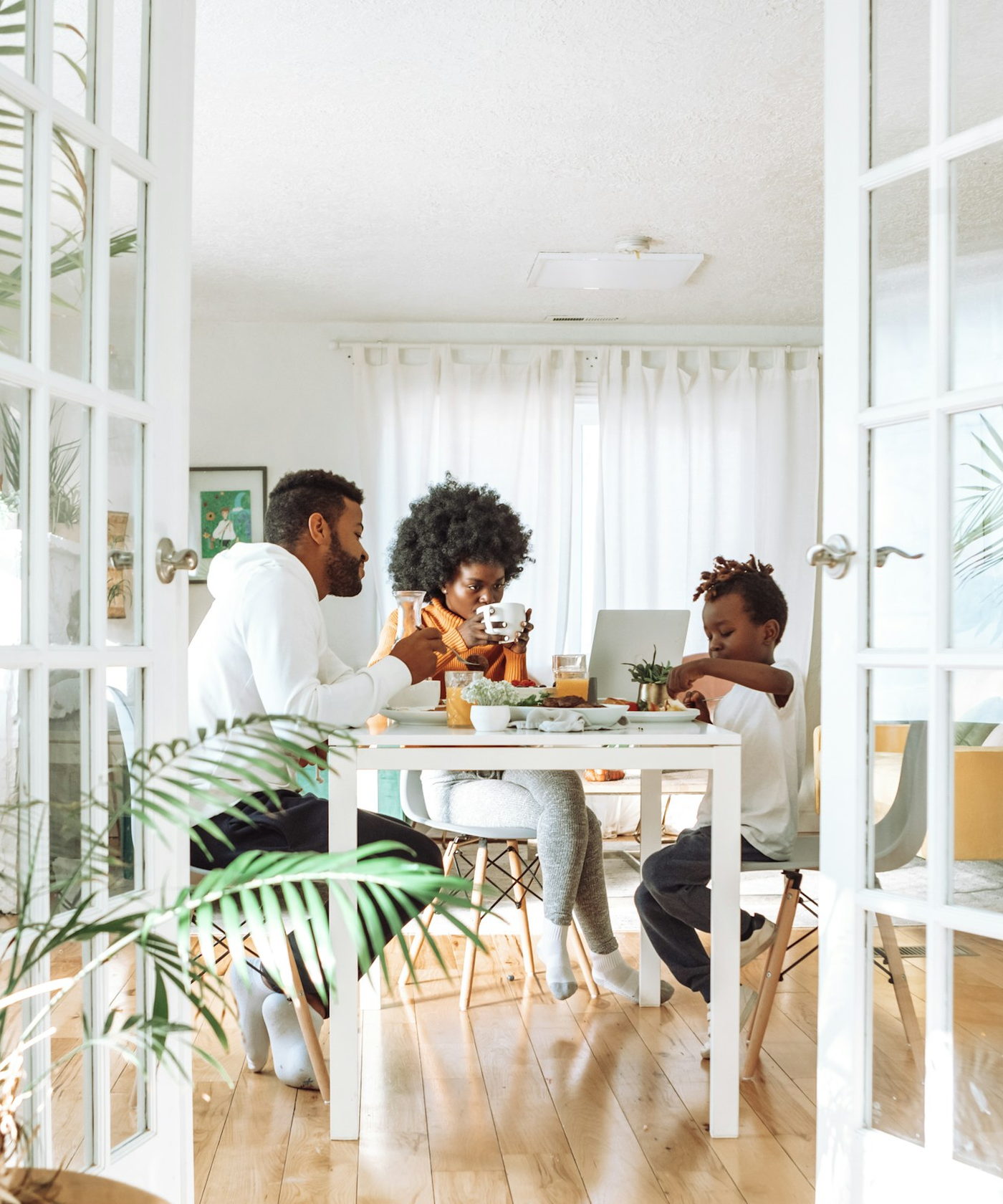 A family sharing a meal at a dining table in a bright home, seen through open doors